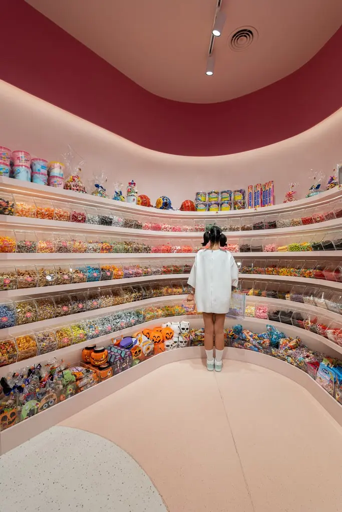 Chica de espaldas mirando una amplia variedad de dulces en estantes coloridos 2 min
