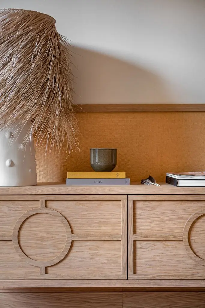un jarron con hierba seca sobre muebles finamente detallados con libros en el interior de un salon con luz natural