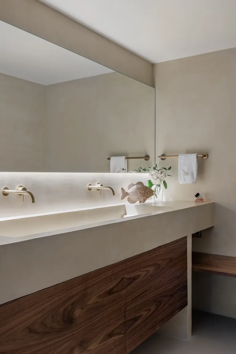 Bano contemporaneo con encimera iluminada grifos dorados y detalles en madera oscura