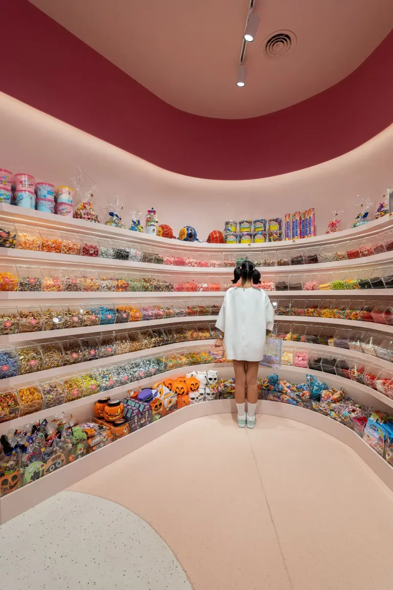 Chica de espaldas mirando una amplia variedad de dulces en estantes coloridos min