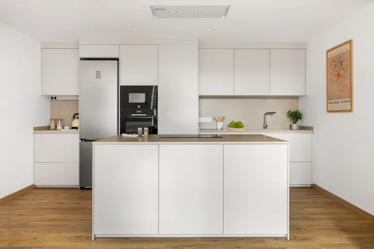 Cocina moderna con armarios blancos nevera de acero inoxidable y suelos de madera