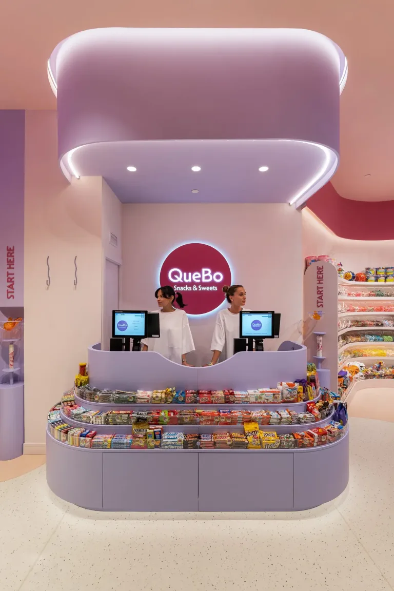 Dos empleadas tras el mostrador de QueBo Snacks Sweets rodeado de golosinas min