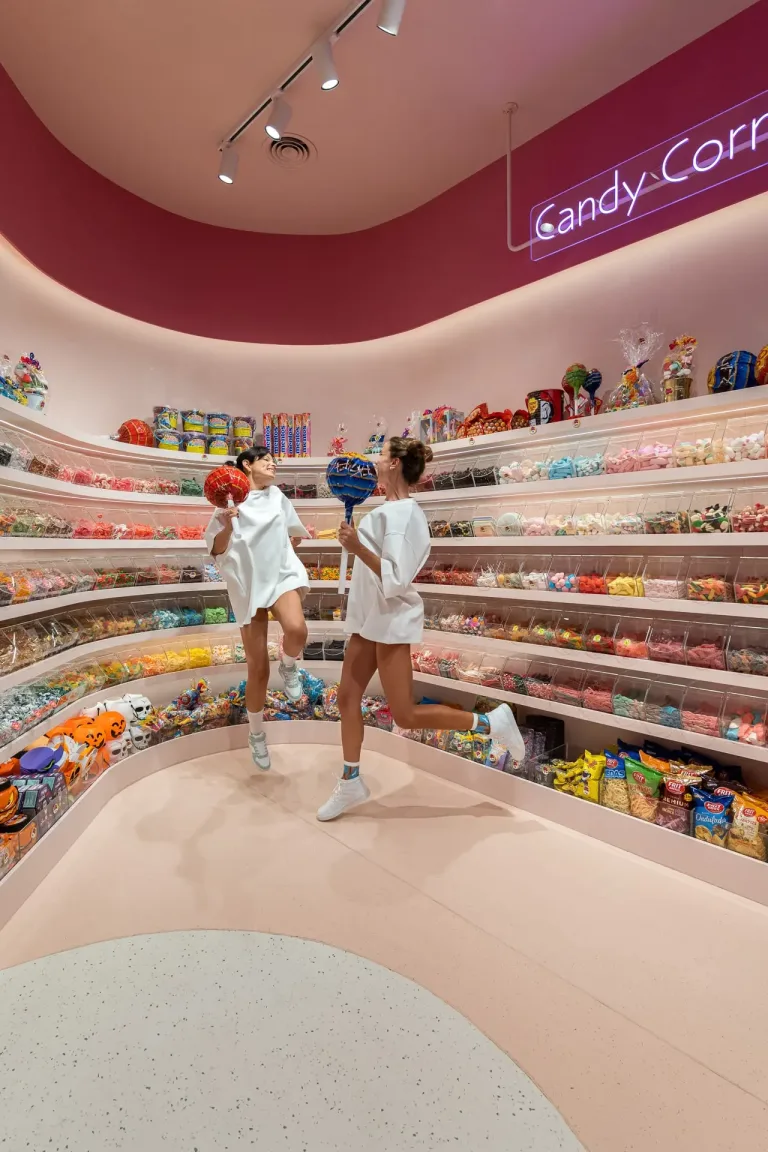 Dos mujeres en Candy Corner sosteniendo grandes paletas y rodeadas de dulces variados min