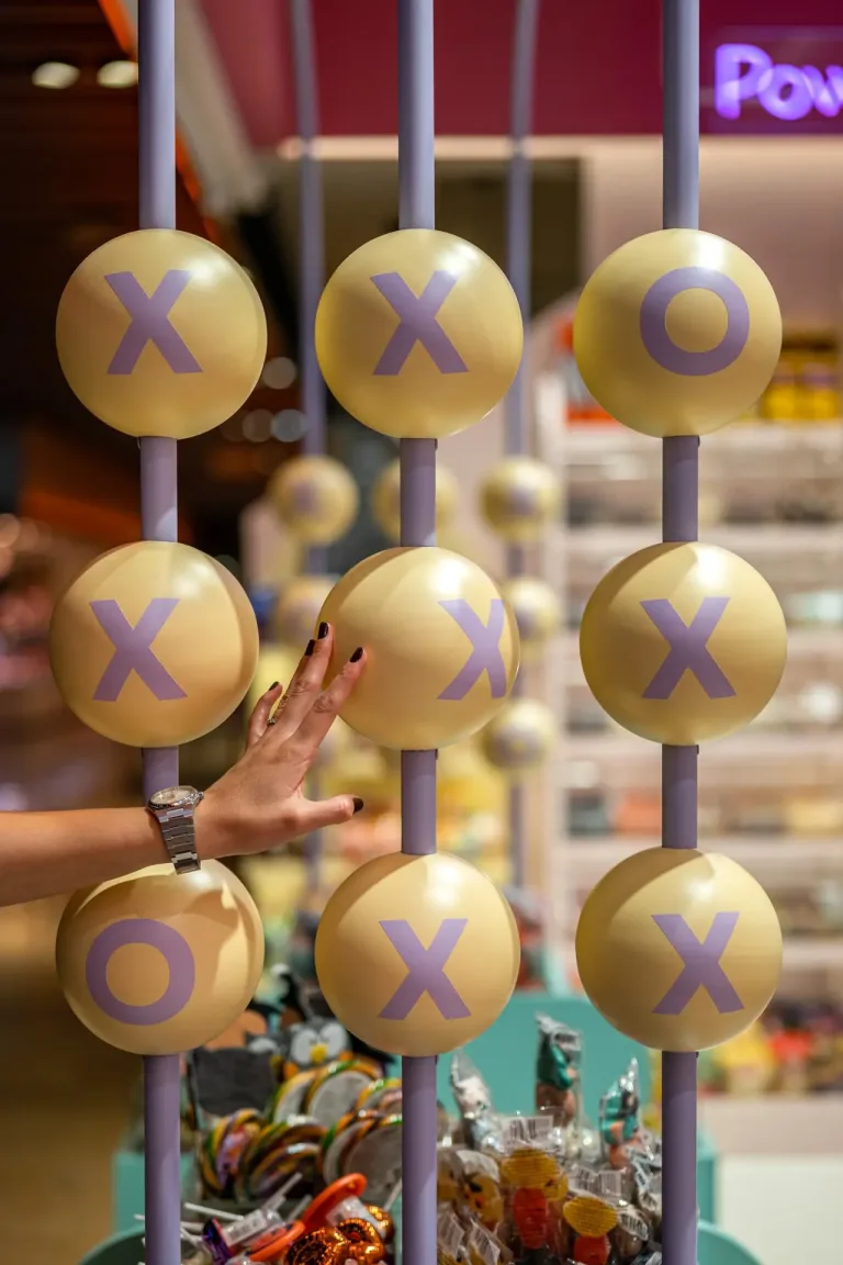 Imagen muestra un juego de tic tac toe gigante con una mano tocando una esfera en una tienda min
