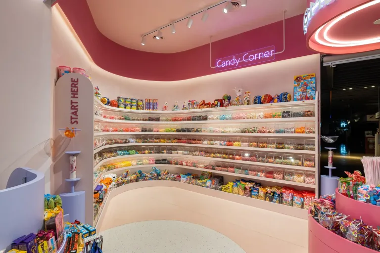 Seccion Candy Corner con variedad de dulces en estantes y senalizacion Start Here en tonos rosados min