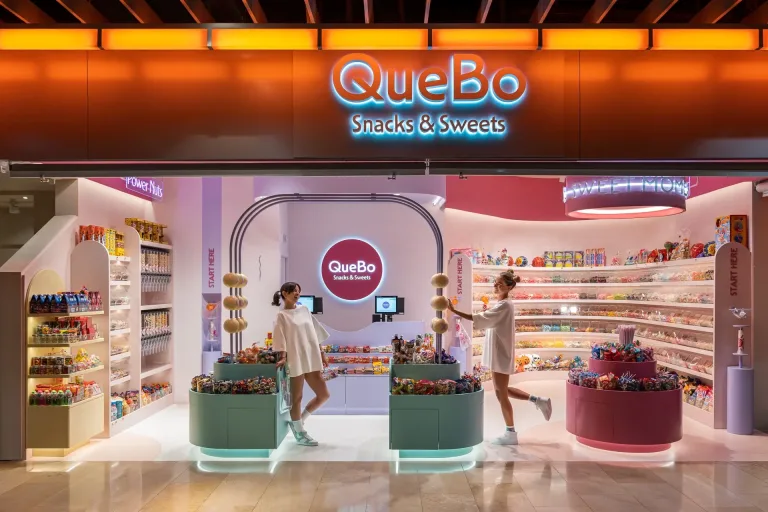 Tienda QueBo Snacks Sweets con dos mujeres explorando dulces y snacks coloridos min