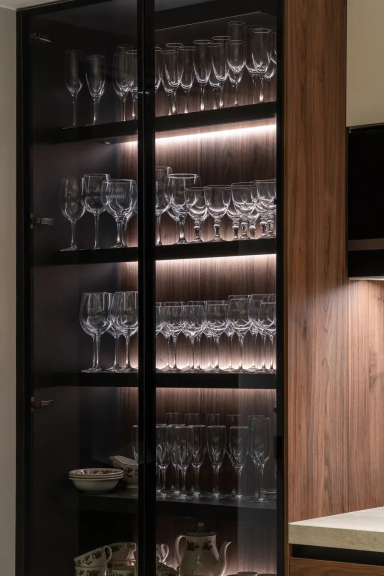 Una elegante vitrina de vidrio con iluminacion interior que resalta una variedad de copas de cristal
