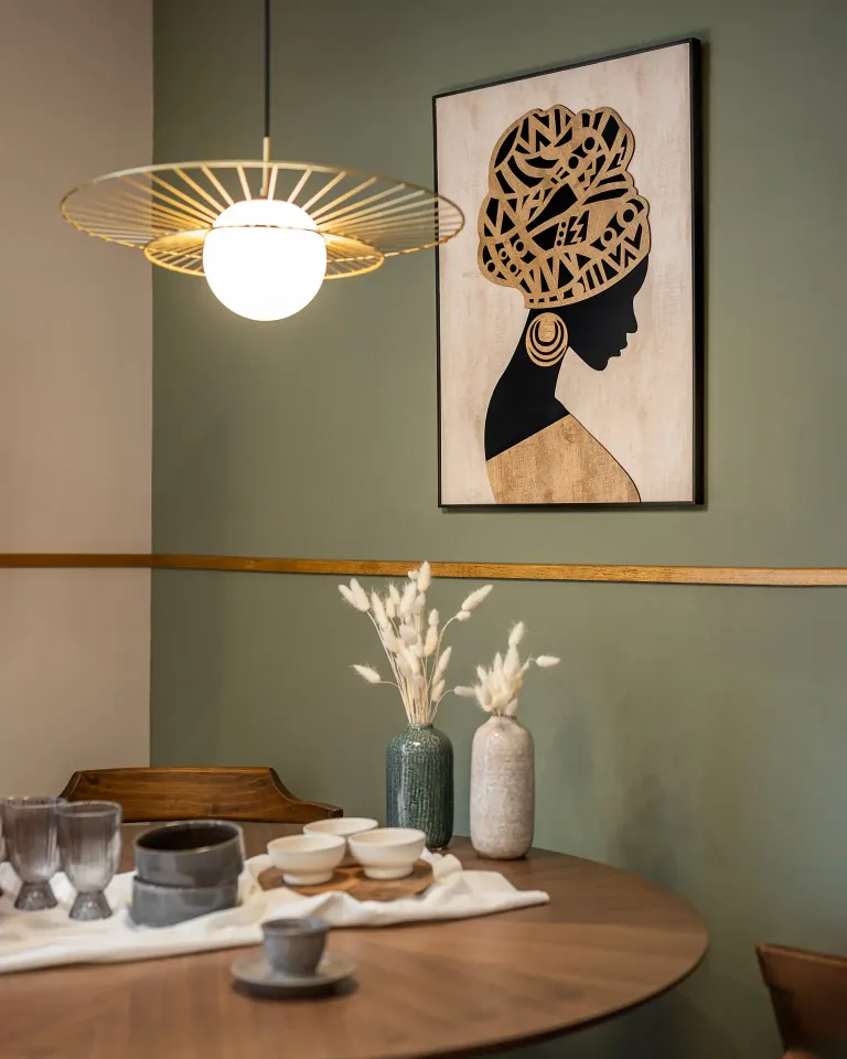 Una obra de arte de una mujer africana realza el interior del comedor con una iluminacion y una disposicion de la mesa elegantes