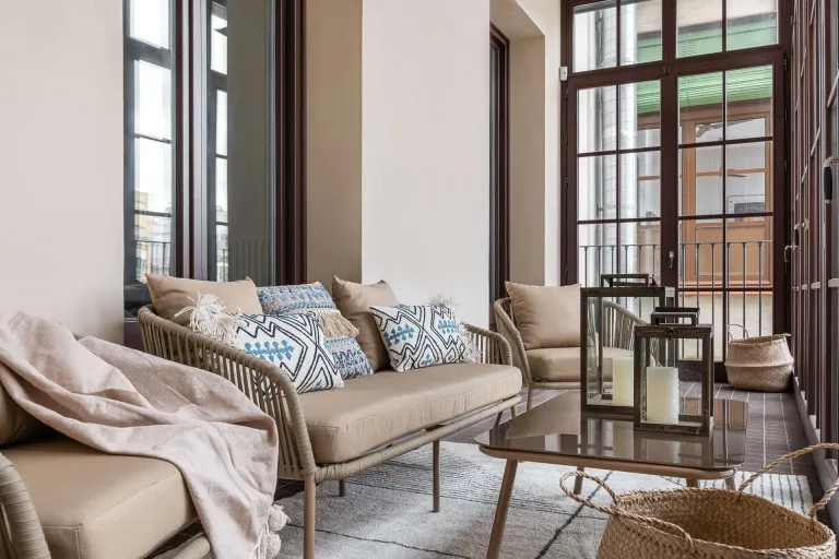 balcon acogedor de un apartamento de la ciudad con un sofa una silla una mesa y una cesta