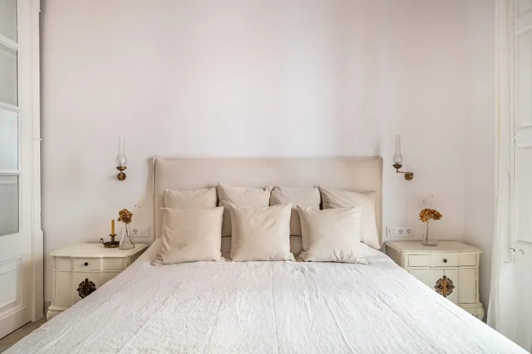 cama con sabanas de lino y muchas almohadas en un dormitorio color crema y blanco
