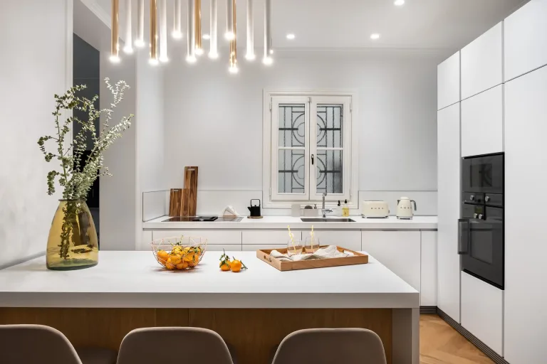 cocina con iluminacion decorativa blanca brillante una isla central con un plato de mandarinas y utensilios de cocina