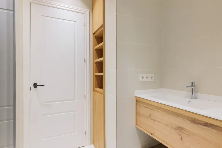 cuarto de bano con armario de madera grifo cromado y lavabo blanco