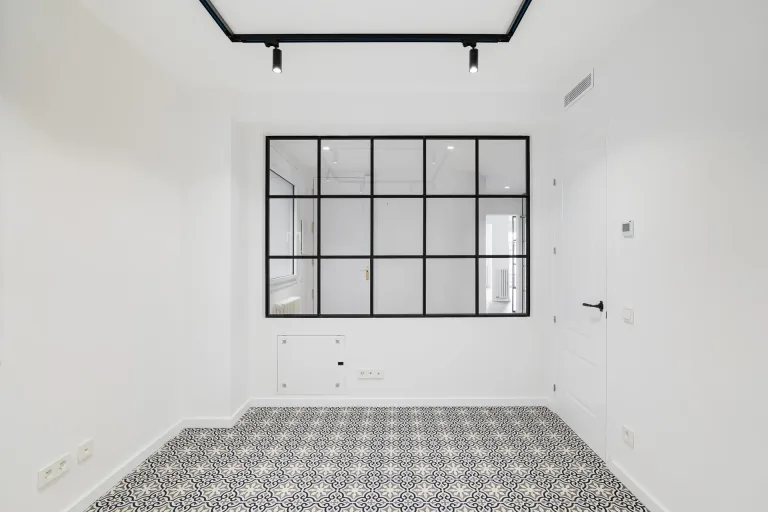 habitacion blanca vacia con una gran ventana y suelo de baldosas