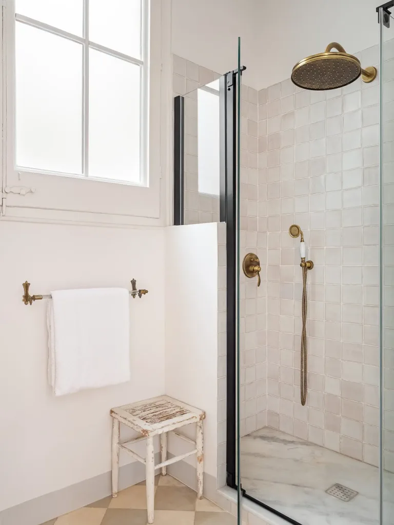 interior de un cuarto de bano con ducha con puerta de cristal y taburete en la esquina