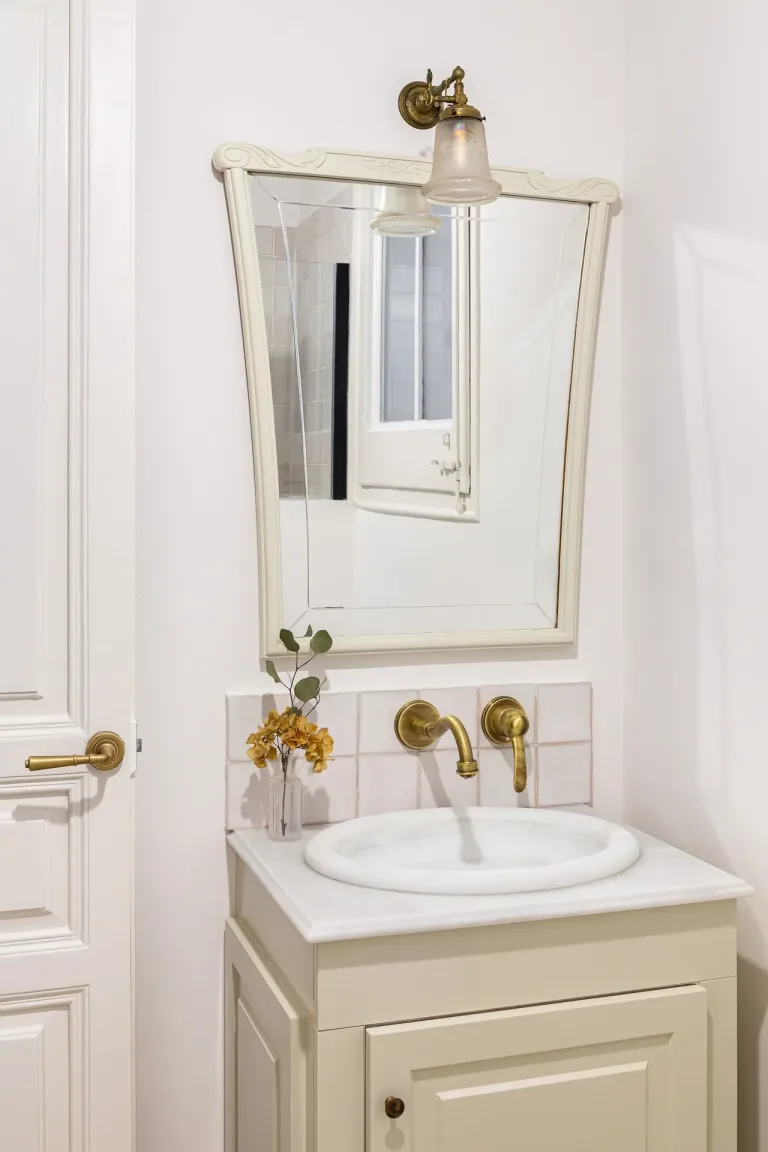lavabo blanco y un espejo en el interior de un bano de color crema