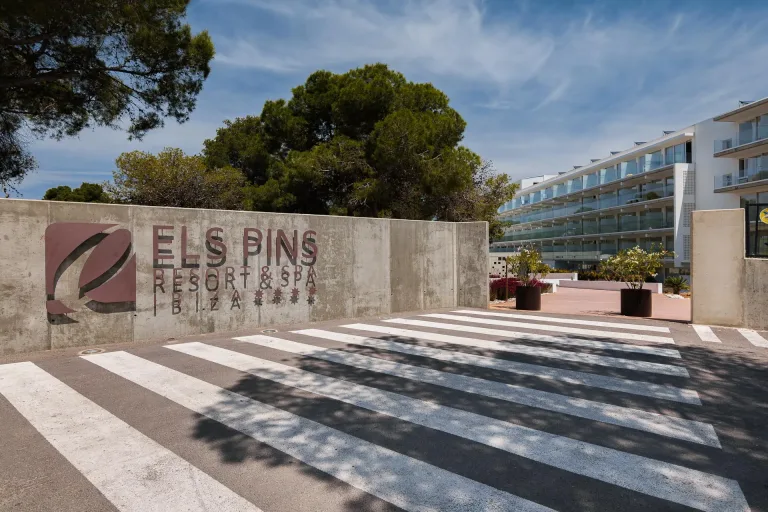 un cartel con el nombre del hotel en un muro de hormigon rodeado de arboles en un dia soleado