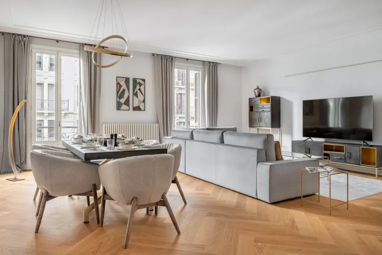 un comedor con mesa y salon al fondo con sofa y televisor en un apartamento moderno