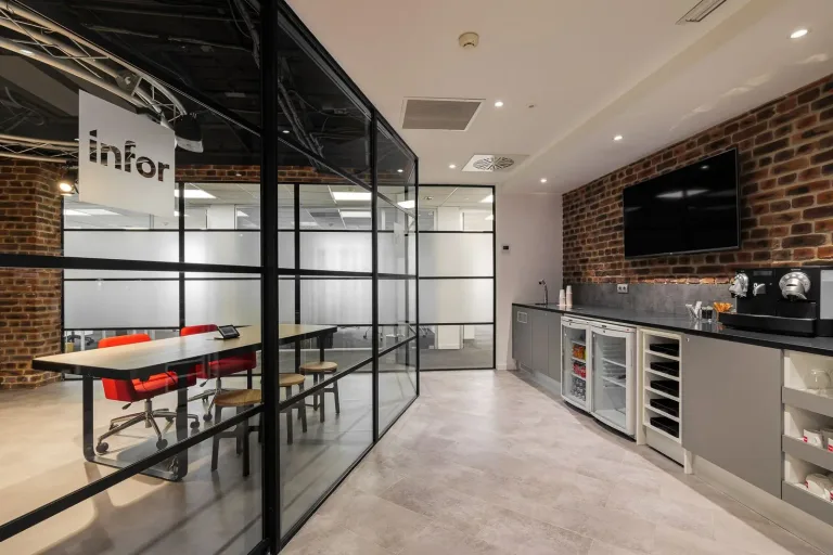 una cocina en una oficina moderna con una pared de vidrio que muestra una sala de reuniones
