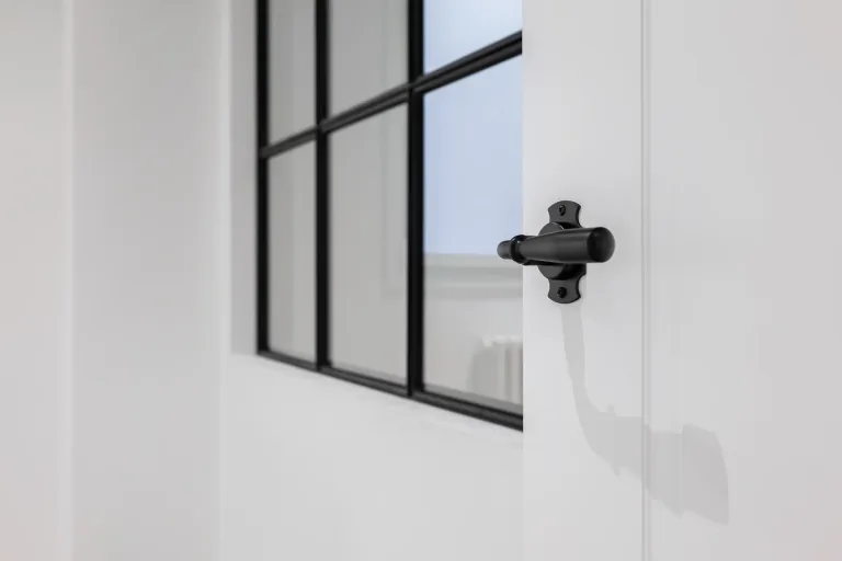 una manija de puerta negra en una habitacion blanca con marco de ventana negro