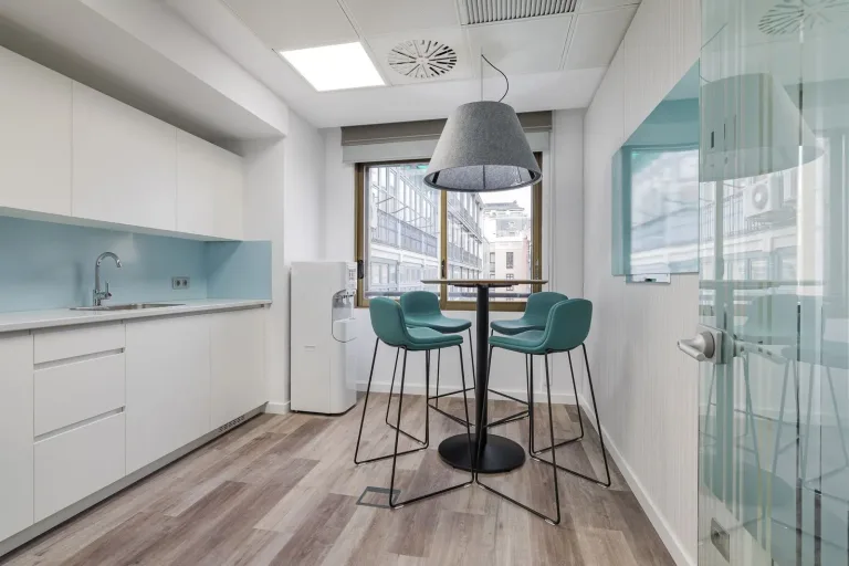 una pequena mesa con sillas azules en una cocina de oficina con ventana