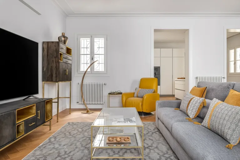 una sala de estar con sofa silla mesa de cafe y television un esquema de color plateado y amarillo