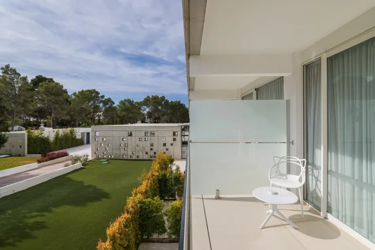 una silla blanca en un balcon con vista a un cesped verde vista desde una habitacion de hotel