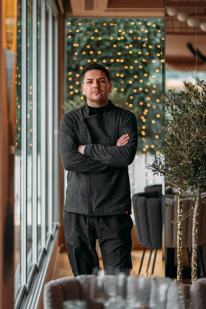 Chef con uniforme negro posando con confianza en un restaurante bien iluminado con luces festivas