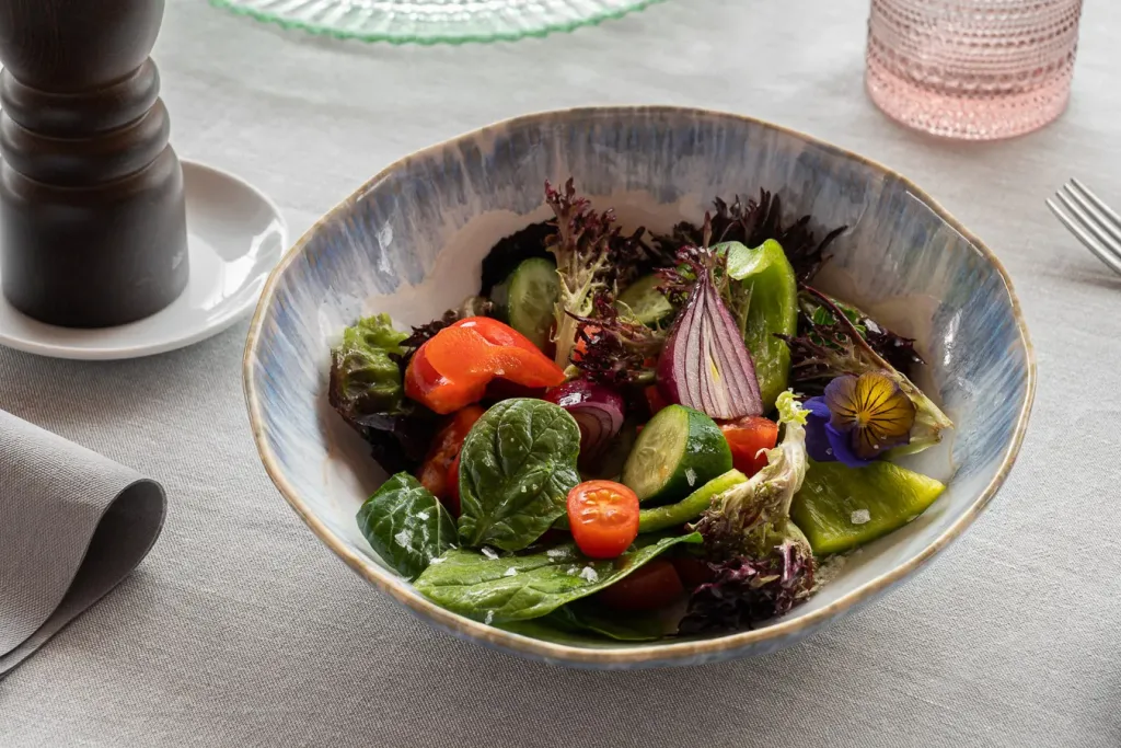 Ensalada vegetal vibrante con flor comestible en un cuenco azul artesanal sobre mantel texturizado