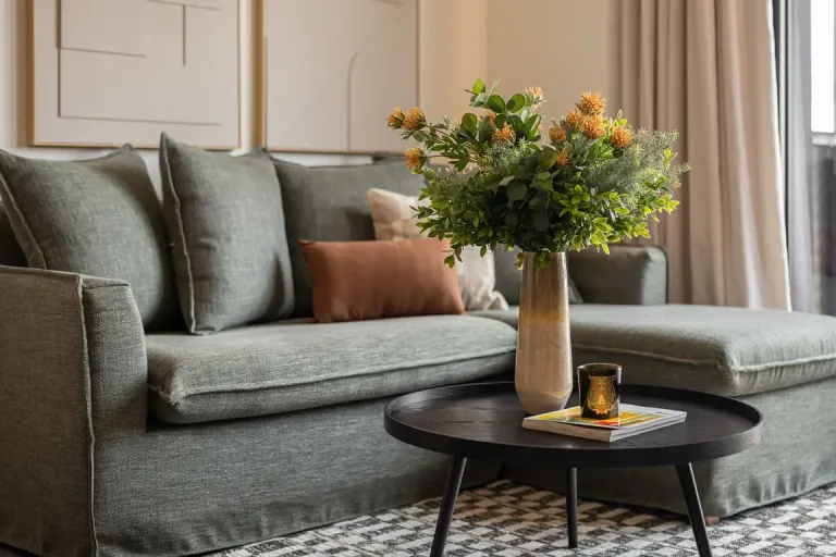 Sala con sofa verde acento en madera y florero sobre mesa cafe