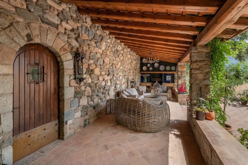porche de piedra con techo de madera y muebles de ratan