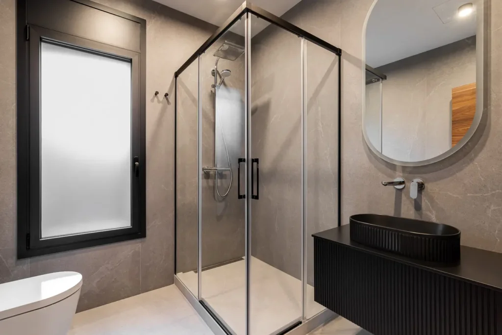 bano moderno con ducha de vidrio lavabo negro y espejo ovalado