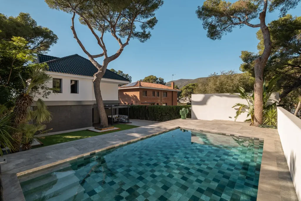 piscina exterior con azulejos verdes rodeada de arboles y casas
