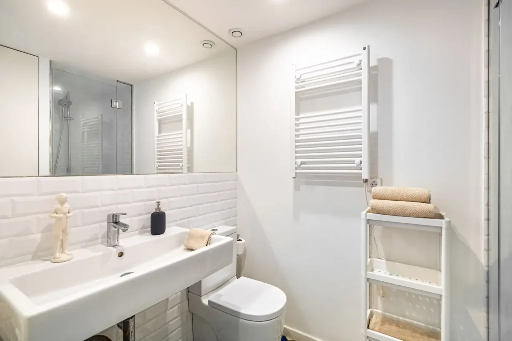 baño moderno minimalista con lavabo blanco espejo grande y ducha de cristal con toallas beige