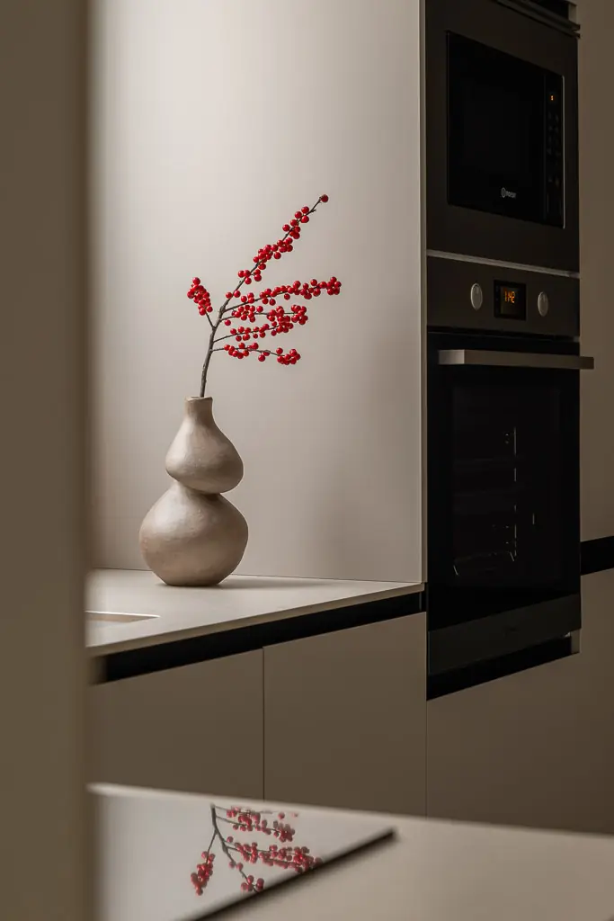 cocina moderna con horno integrado y jarron con ramas rojas
