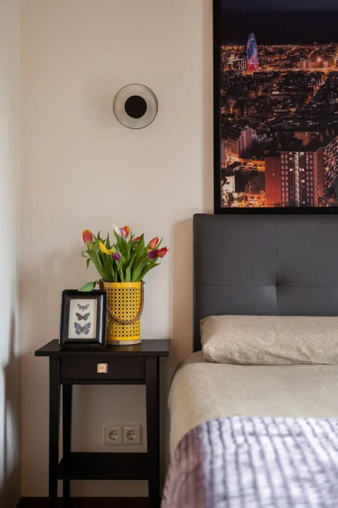 dormitorio con mesita negra flores y cuadro de ciudad nocturna