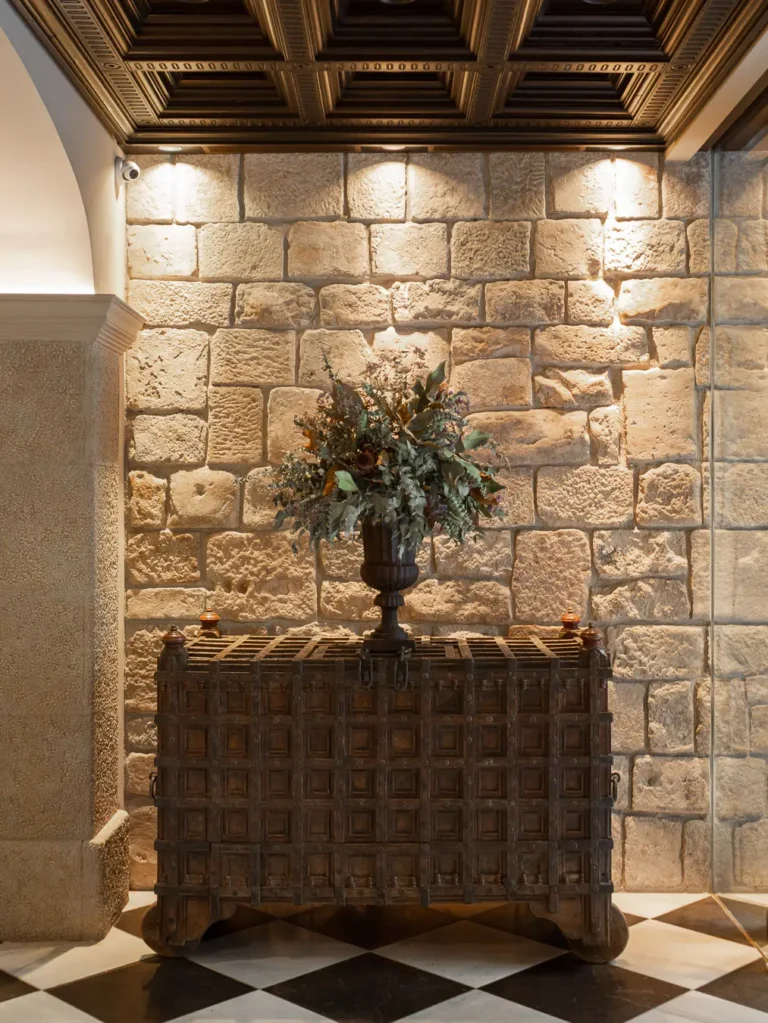 arcon de madera tallada con arreglo floral ante pared de piedra