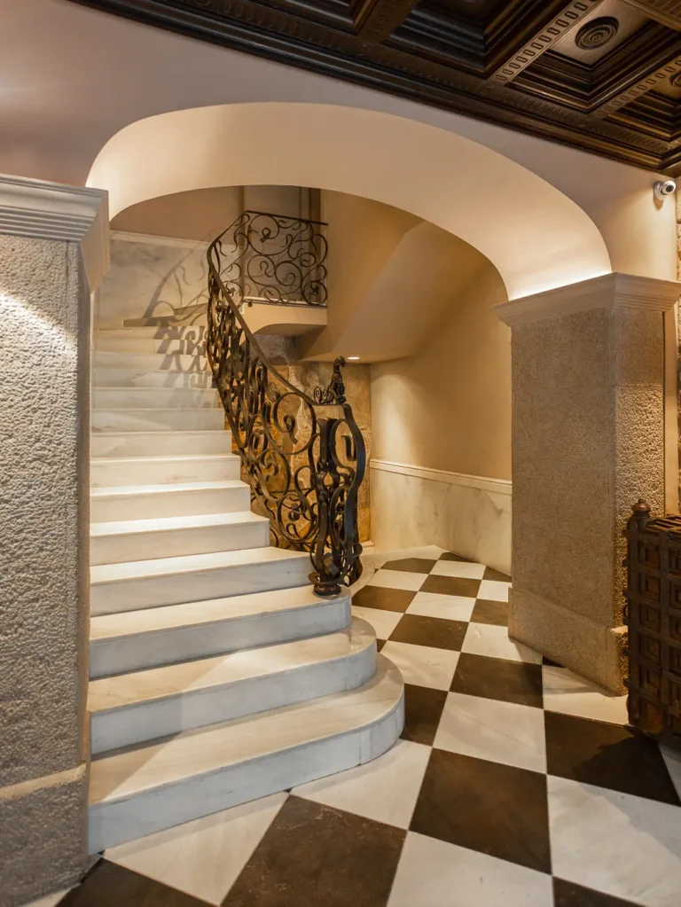 escalera de marmol blanco con barandilla de forja bajo arco
