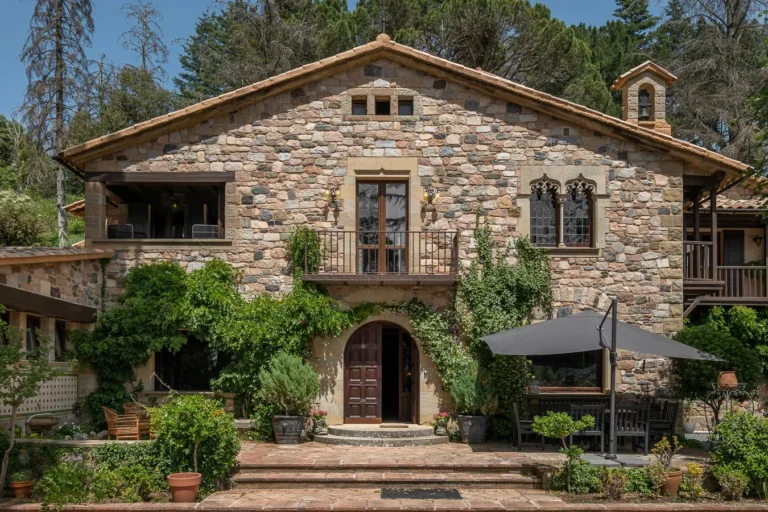 fachada de casa rustica de piedra con balcon y terraza ajardinada