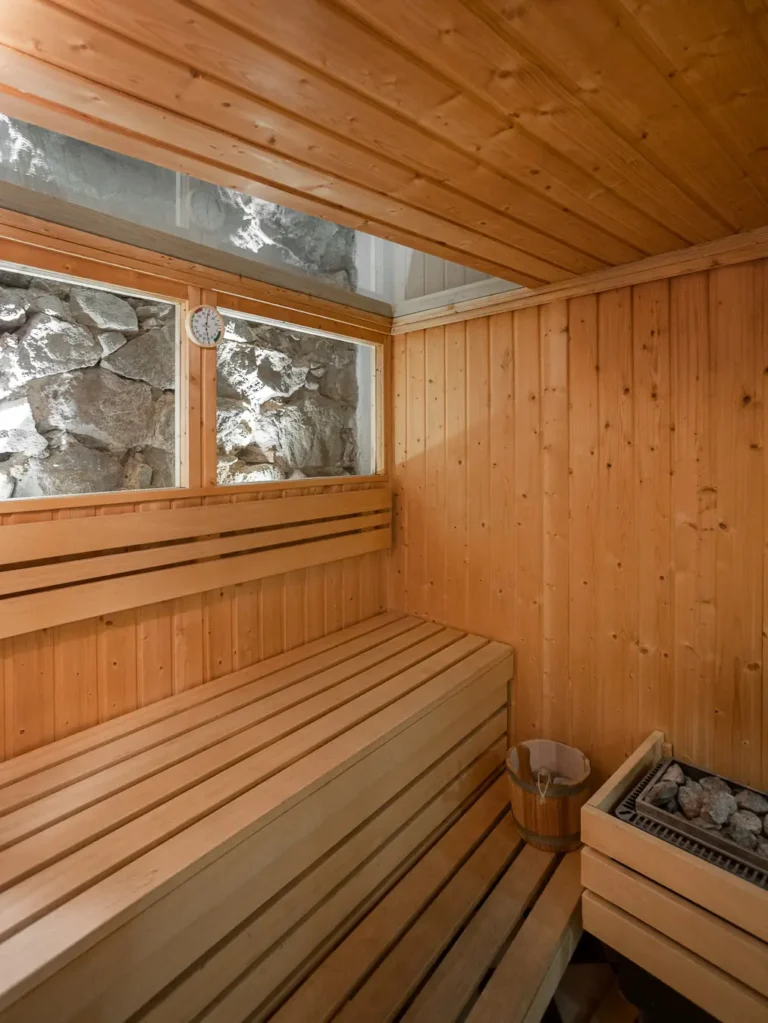 interior de sauna de madera con bancos estufa de piedras y ventanas