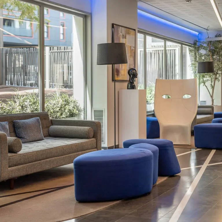 lobby con sofa gris y pufs azules junto a ventanales