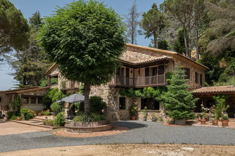 vista lateral de casa de piedra con porche de madera y arboles